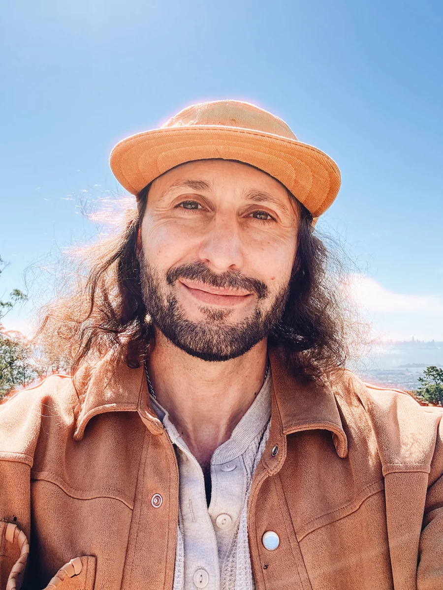 Jordan Michael Moon Schuster, founder of Omega Mega, in a wide-brimmed hat and a tan leather jacket.